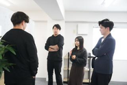 オフィスでのミーティング風景。ホワイトボードに書き出した課題に対し、メンバー全員で意見を出し合いながら進捗を確認している様子です。