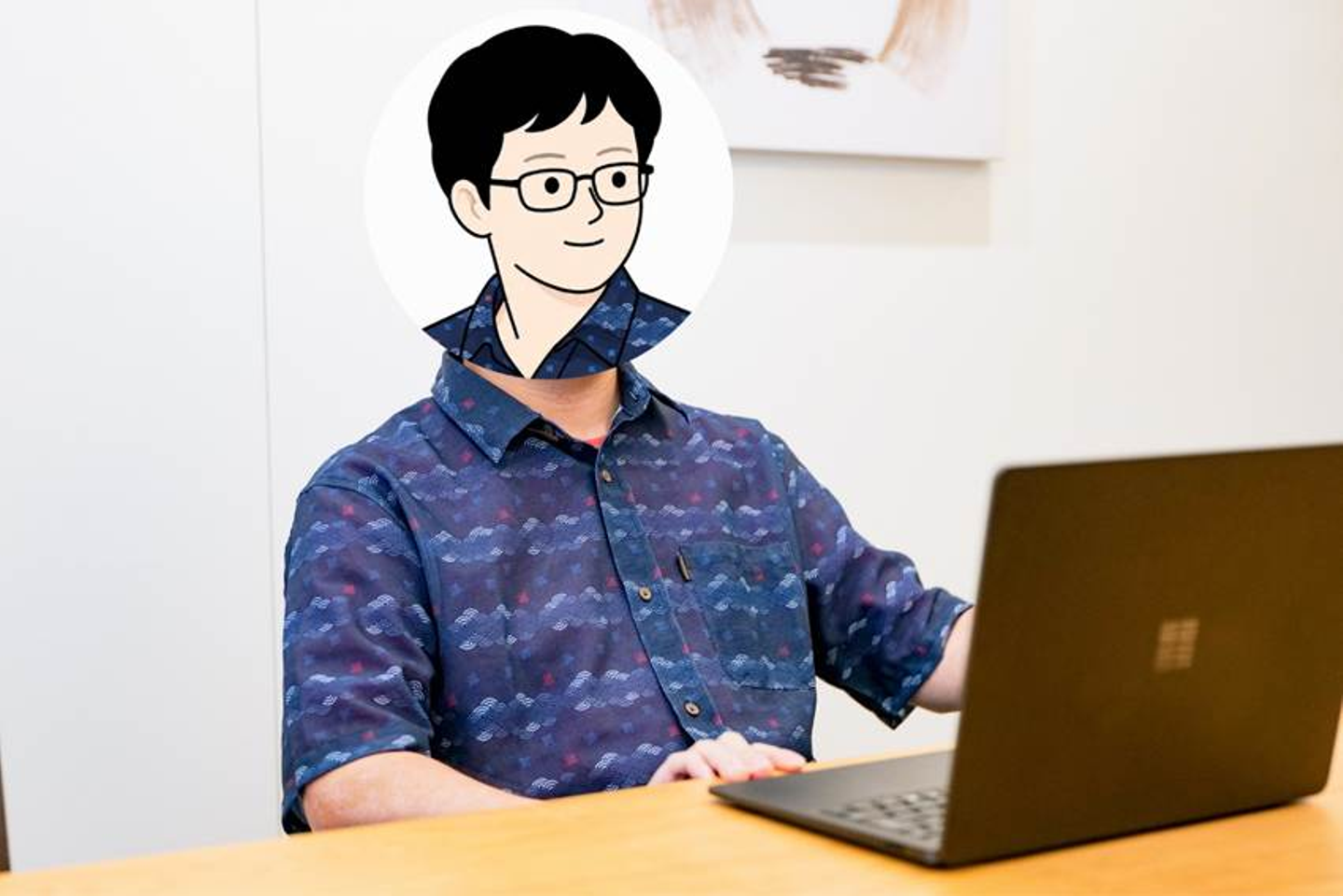 The image shows a person wearing a plaid shirt and a black hoodie, seated at a desk with a laptop open, and a white wall with a framed picture behind them.

AI 生成コンテンツは誤りを含む可能性があります。