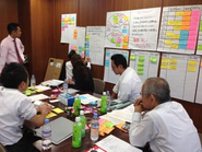 企業様内での会議の一例です。コーチはピンクのシャツの人です。おやつや飲み物があり、付箋が用いられて会議を進めます。