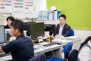 PCに向かって事務作業を進める先輩社員の様子です。お客様に最適な提案をするための資料作成や、機械が安全に動くためのメンテナンス計画のサポートなど、多岐にわたる業務を行っています。私たちの仕事は、お客様の「困った」を解決し、快適な環境を提供すること。 そのためには、地道な事務作業もとても大切です。入社後は、基本的なPC操作から丁寧に教えますので安心してください。お客様第一に考える姿勢を大切にするこの職場で、私たちと一緒に、社会人として大きく成長していきましょう！