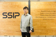 オフィスのパーティションの前にて。特許事務所らしくないオフィスの内装です。服装規定は特にありません。カジュアルでOKです。